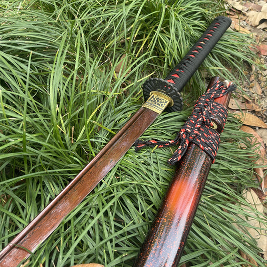The Inferno Blade Katana with its "Folded Red" 1095 steel blade and speckled lacquer saya, displayed outdoors.