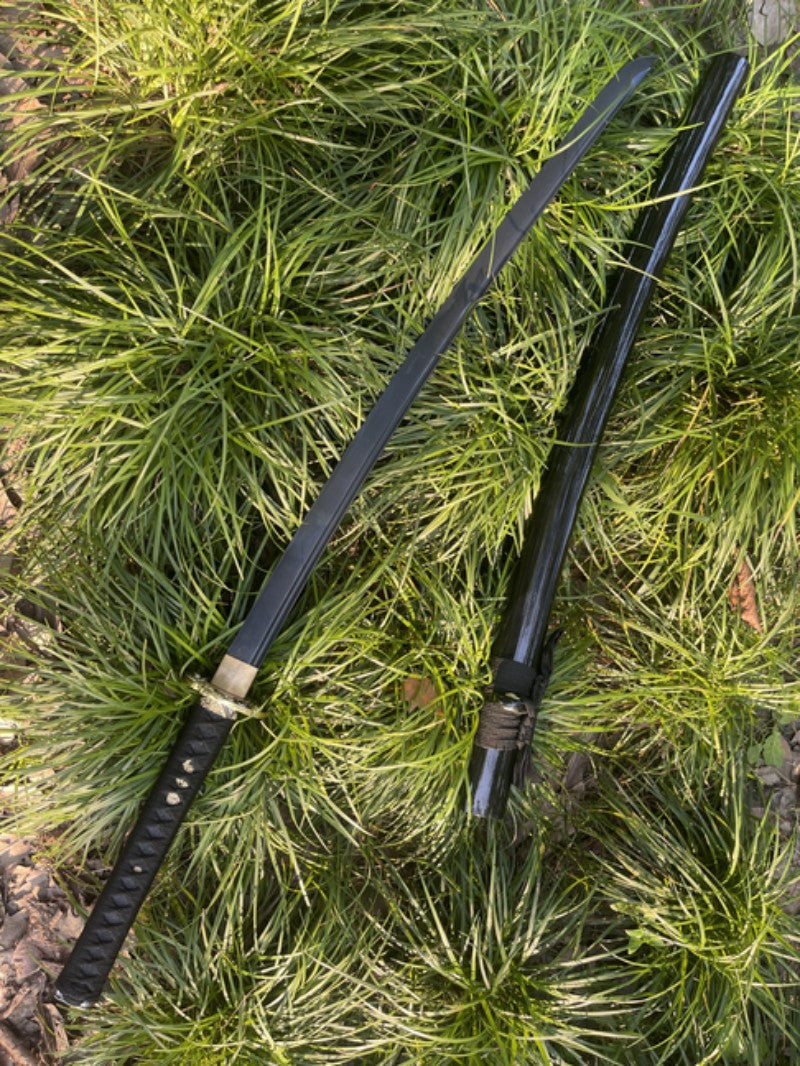 The unsheathed Obsidian Edge Katana and its saya lying side-by-side on a bed of grass.