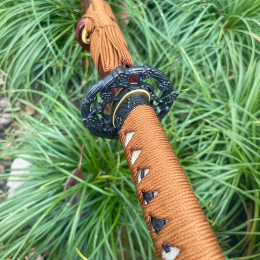 A close-up of the tsuka handle, featuring the brown synthetic-silk ito wrap and floral-themed fittings.
