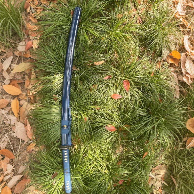 The complete Abyss Fang Katana, fully sheathed in its deep-blue gloss lacquer saya, resting in the grass.