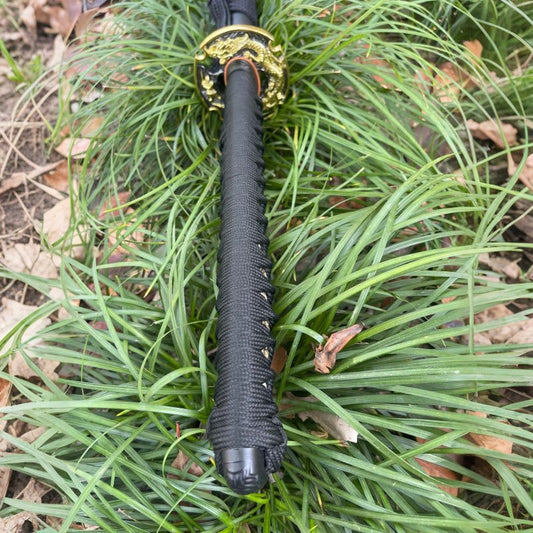 A close-up of the tsuka handle, featuring a black silk ito wrap and the "Dragon vs. Samurai" theme tsuba.