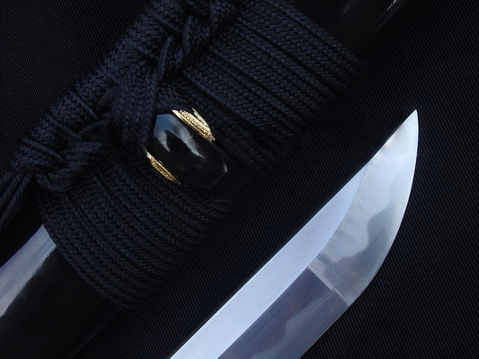A close-up of the Kiku's Reflection Katana, showing the mirror-polished 1095 steel kissaki (tip) next to the high-gloss black saya.