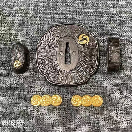 Complete Koshirae set featuring the gilded Mitsu Tomoe symbol on a textured, dark-patinated brass Tsuba, Fuchi, Kashira, and Menuki.