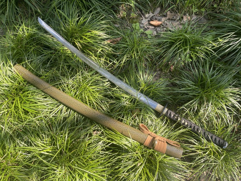 The unsheathed Forest Viper Katana and its saya displayed in a grassy, outdoor environment.
