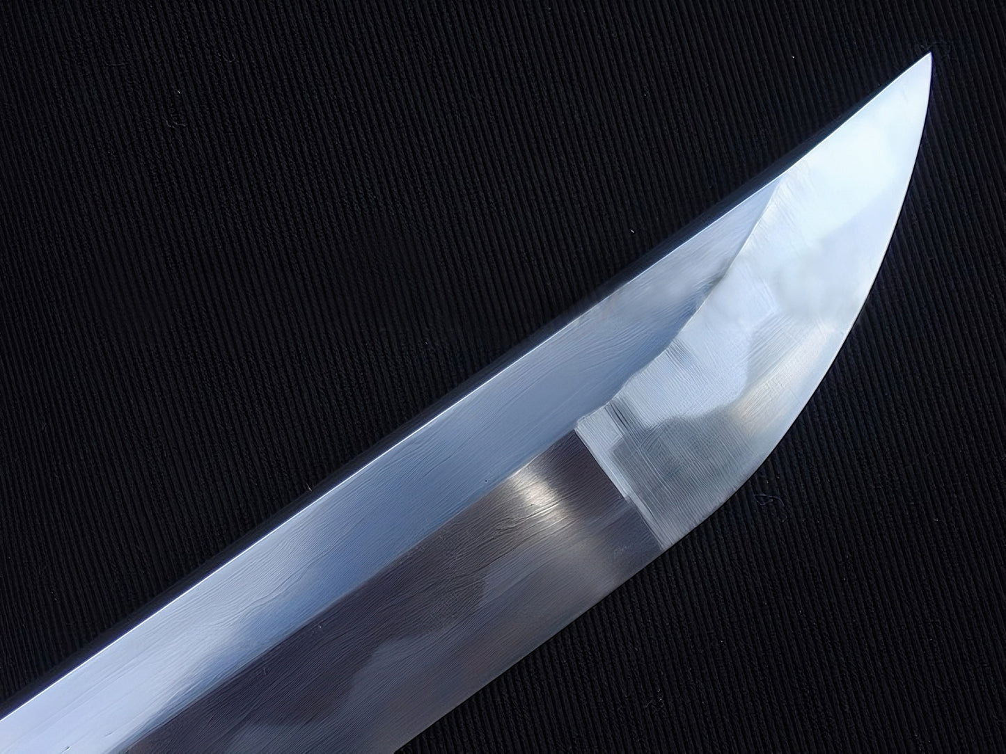 A detailed macro shot of the chu-kissaki tip, highlighting the flawless hand-polished mirror finish on the 1095 steel blade.