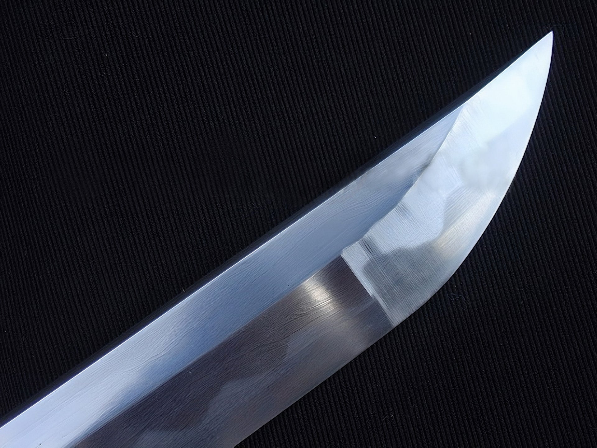 A detailed macro shot of the chu-kissaki tip, highlighting the flawless hand-polished mirror finish on the 1095 steel blade.
