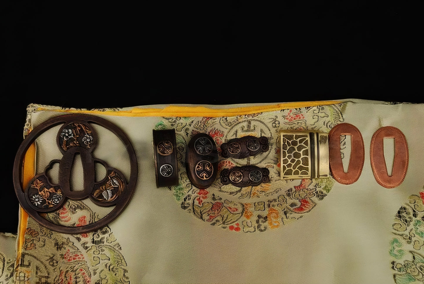 An overhead view of the complete set of antique copper, gold and silver gilded "Mitsudomoe" theme fittings for the Gilded Tomoe Katana.