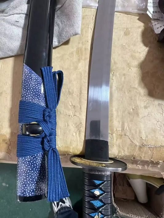 Custom blue rayskin katana — black lacquer saya with blue cord beside the drawn blade and gold wolf tsuba
