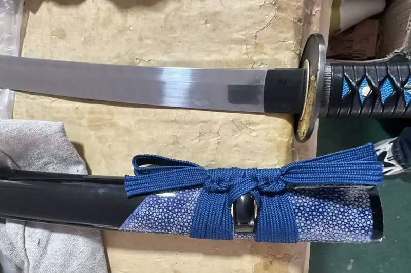 Custom blue rayskin katana — black lacquer saya with blue cord beside the drawn blade and gold wolf tsuba.