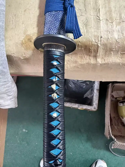 Black ito wrap over blue rayskin handle with gold wolf menuki — tsuka close-up
