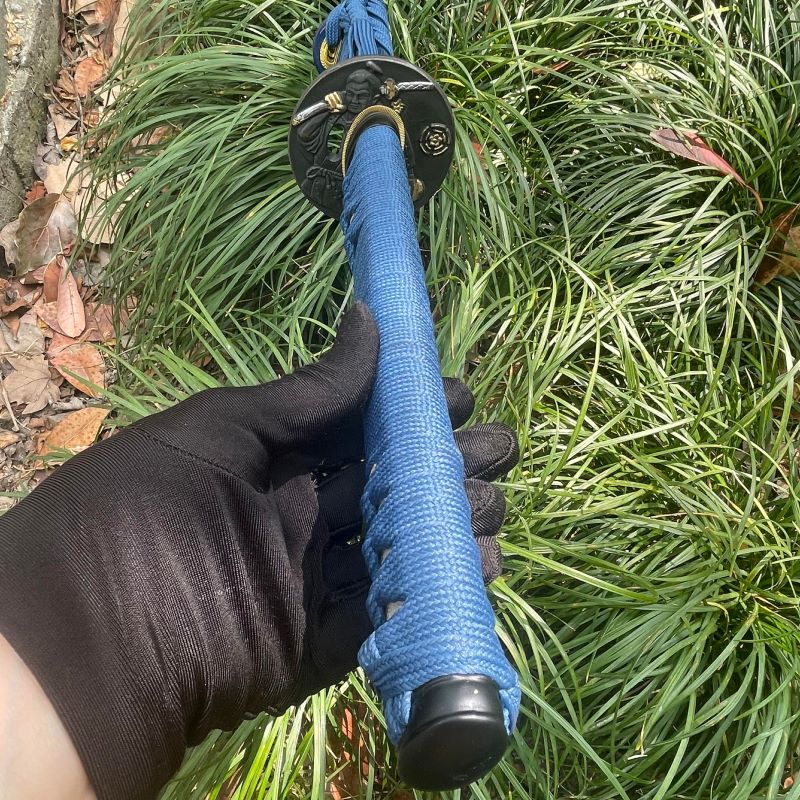 The handle of the Abyss Fang Katana being held by a gloved hand, showing the blue synthetic-silk ito wrap.