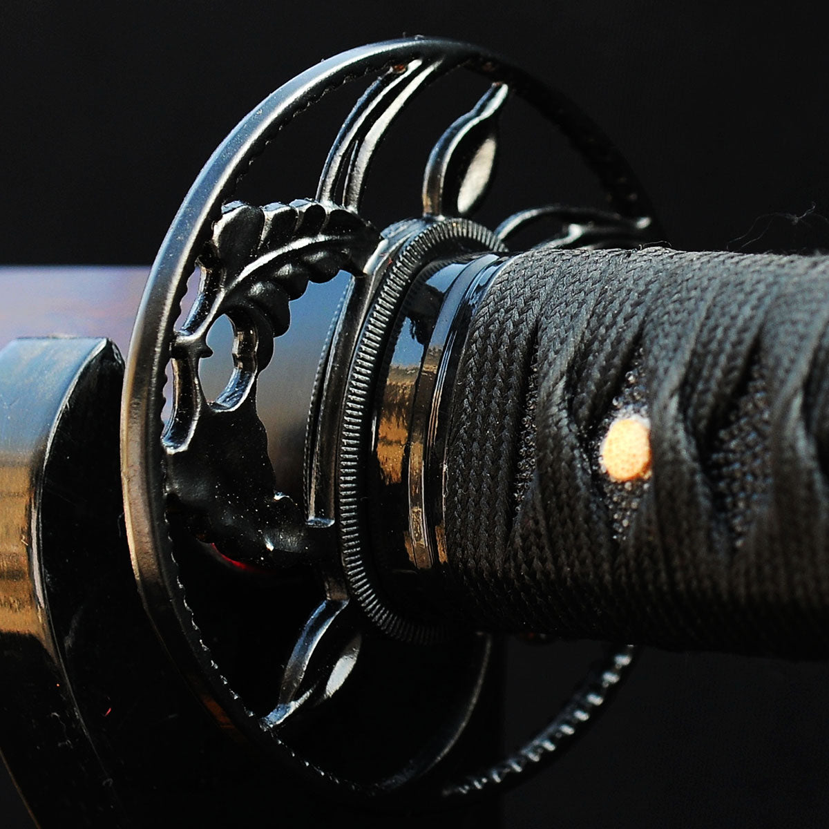 A detailed macro shot of the Kuro Akane Katana's iron tsuba, featuring the elegant sukashi (openwork) design of coiling botanical vines.