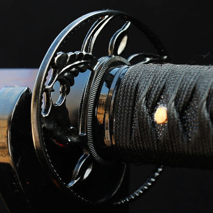 A detailed macro shot of the Kuro Akane Katana's iron tsuba, featuring the elegant sukashi (openwork) design of coiling botanical vines.