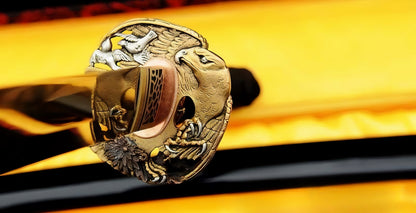 A close-up of the Golden Hawk Katana, showing the intricate brass habaki and the "Golden Hawk" theme fuchi (hilt collar) at the base of the handle.