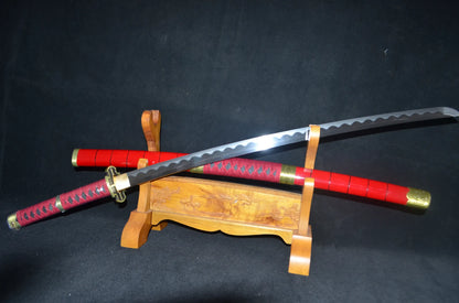 The Sandai Kitetsu katana drawn at an angle, showing the wavy clay-tempered hamon on its polished blade above the red saya and wooden stand.