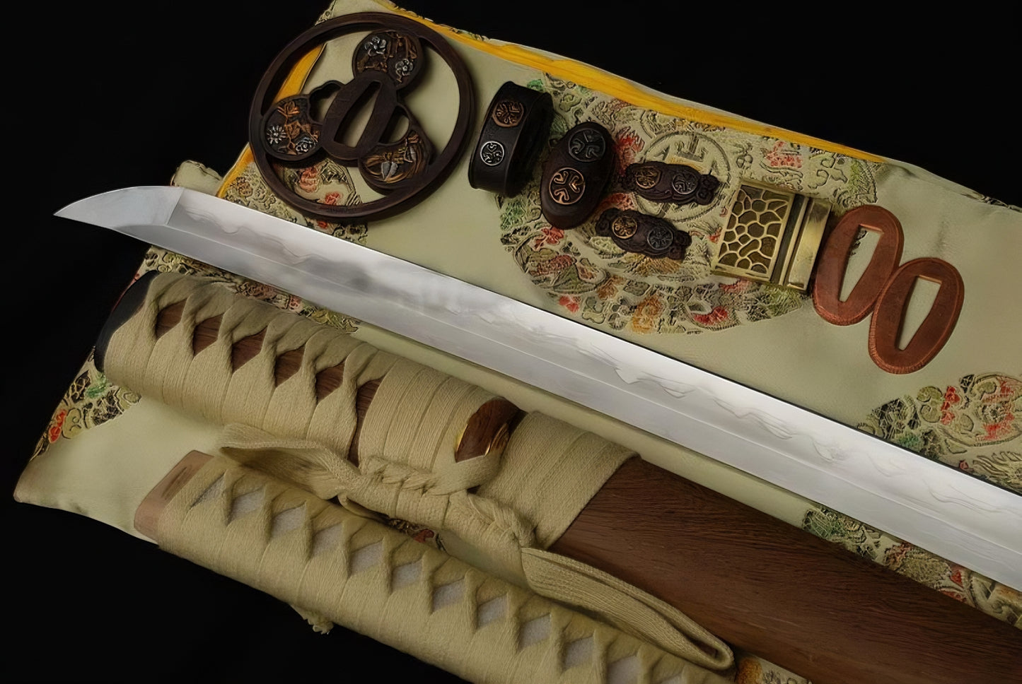 The folded 1095 steel clay-tempered blade and beige-wrapped handle of the Gilded Tomoe Katana, displayed with its gilded "Mitsudomoe" fittings.