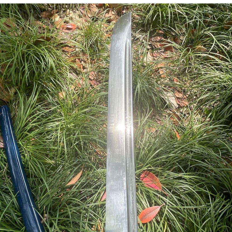 A full view of the unsheathed 1095 folded steel blade of the Abyss Fang Katana, resting in a bed of grass.