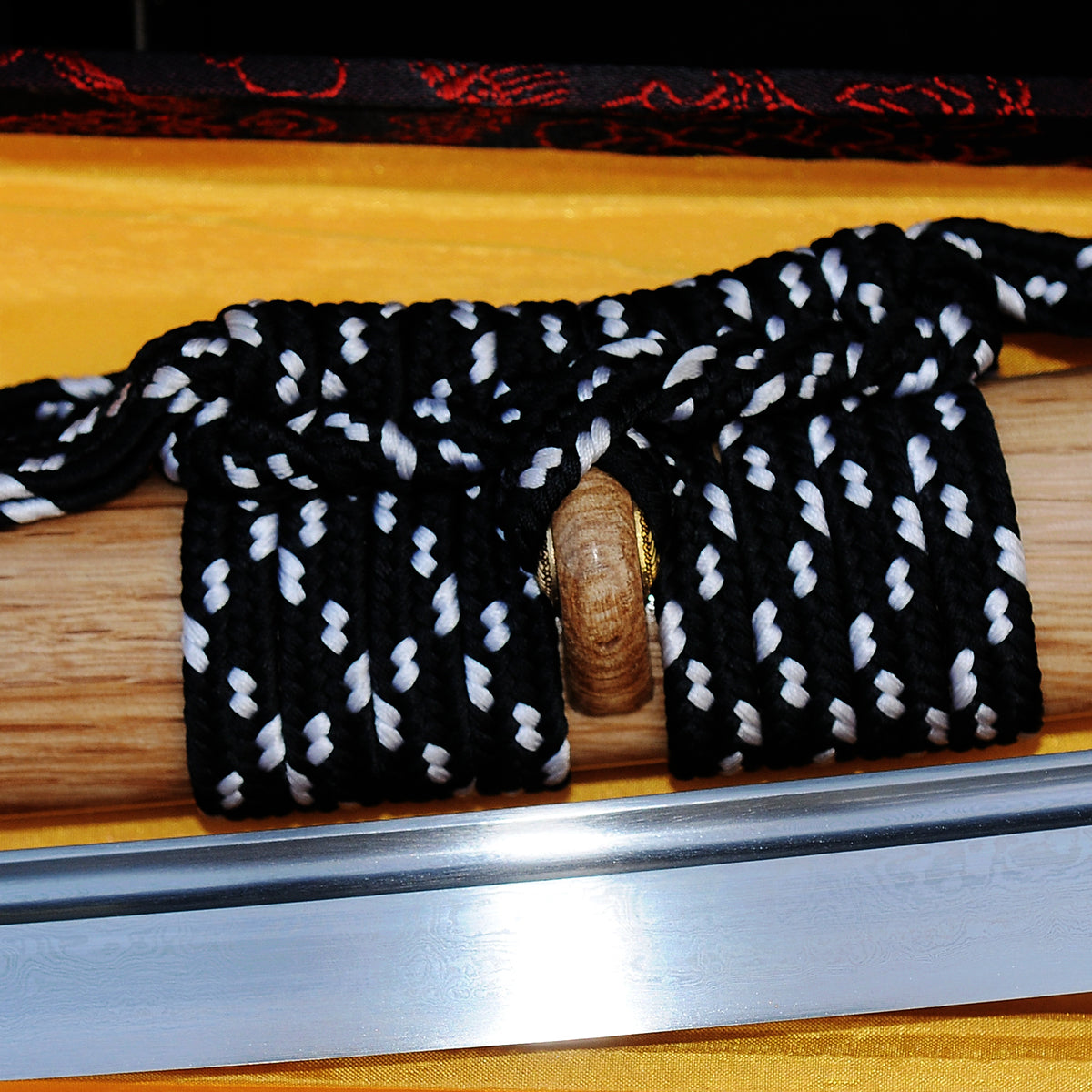 A close-up of the Taka's Sky Katana, showing the folded 1095 steel blade's grain (jihada) next to the natural hardwood saya and its sageo cord.