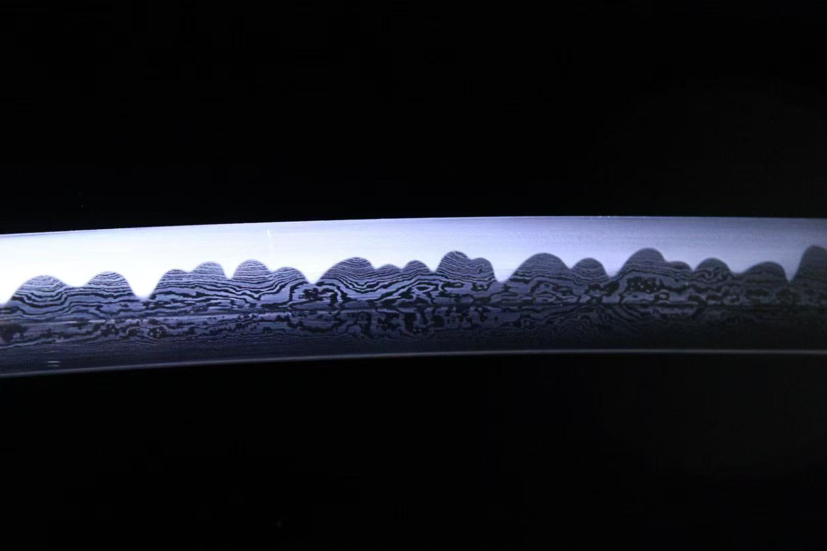 A bright macro shot of the blade, revealing both the folded steel pattern (hada) and the clay-tempered hamon.