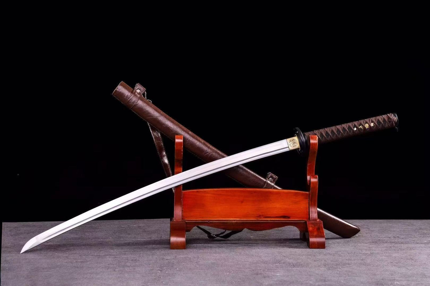The Dusklight Fang Katana, featuring a hand-forged folded steel blade and a brown leather saya, on a display stand.