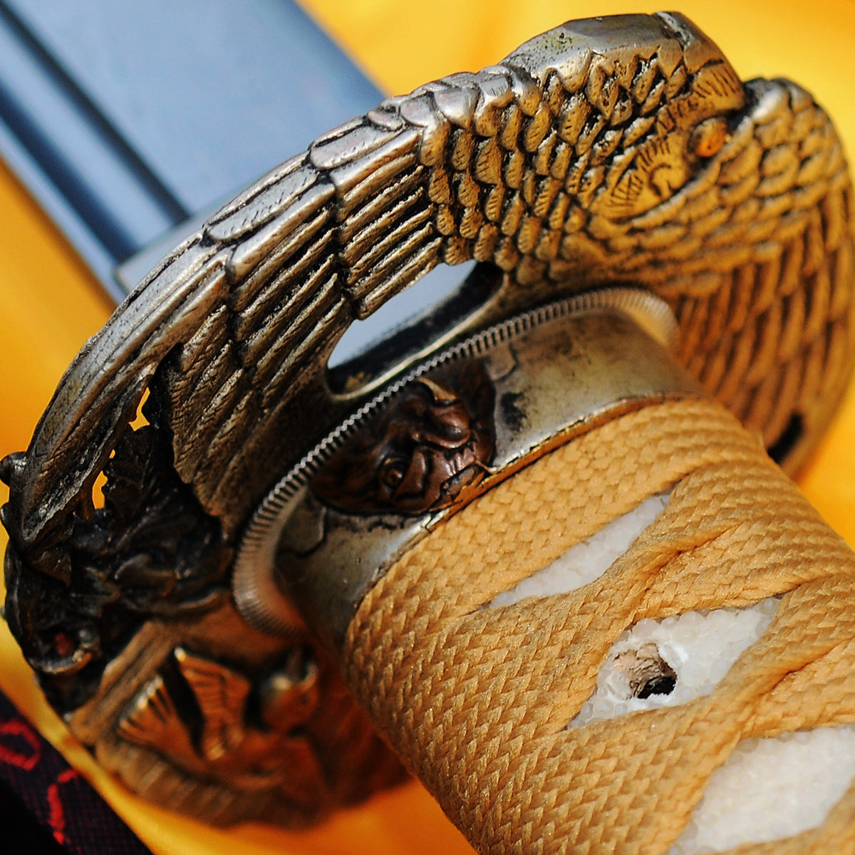 A close-up of the Taka's Sky Katana's handle, showing the gold/tan cord ito wrap over white genuine rayskin and the copper "Taka" (Eagle) theme fuchi.