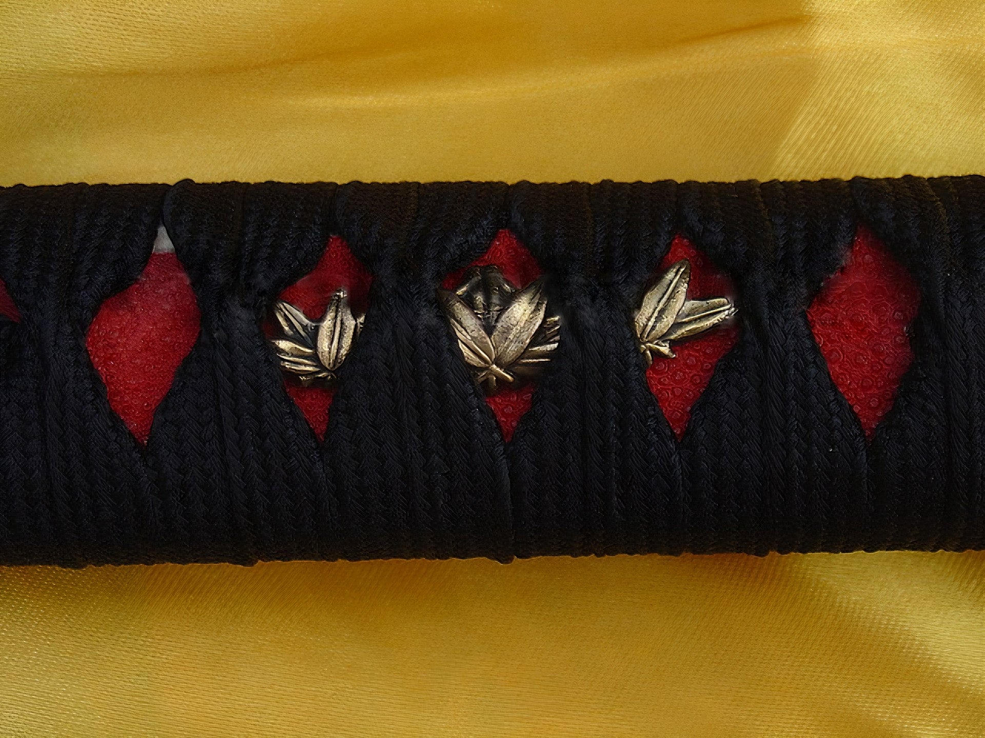 A macro shot of the Kiku's Reflection handle, showing the golden maple leaf (Momiji) menuki over red genuine rayskin.