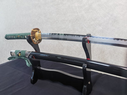 A close-up of the tsuka handle, showing the green silk ito wrap and the brass serpent theme tsuba.