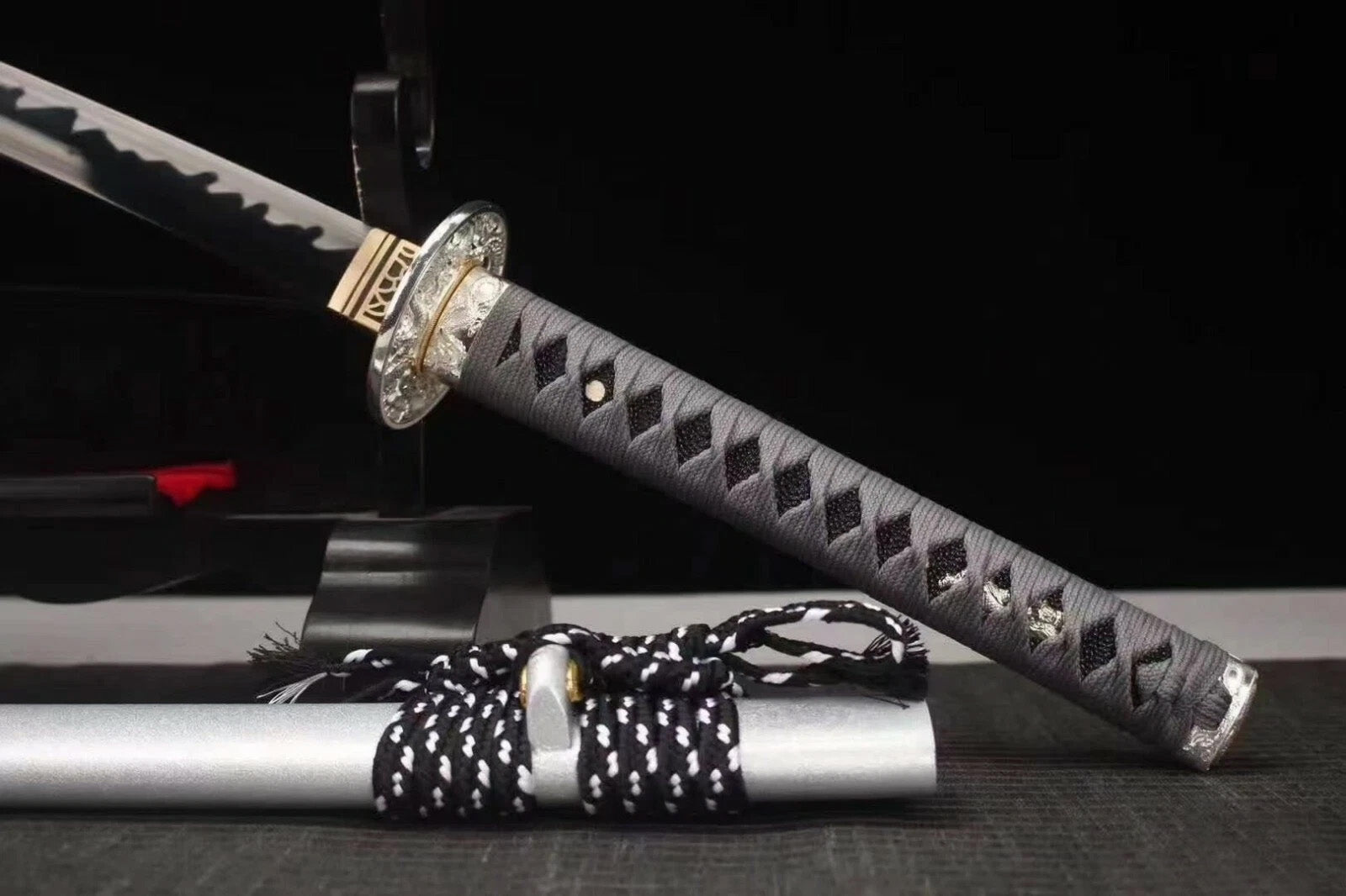 A close-up of the tsuka handle (grey ito wrap) and the upper part of the matte silver saya.