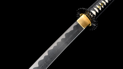 Folded 1095 steel nodachi blade showing the wood-grain hada and notare hamon, with brass habaki and black iron tsuba.
