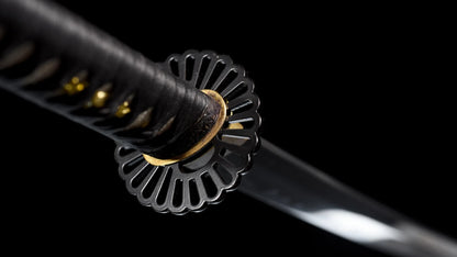 Black iron chrysanthemum sukashi tsuba on the folded steel nodachi — close-up.