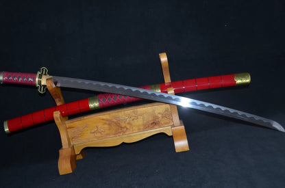 Close angled view of the Sandai Kitetsu katana, its open-work gold tsuba and red-wrapped tsuka beside the polished blade and wavy hamon.
