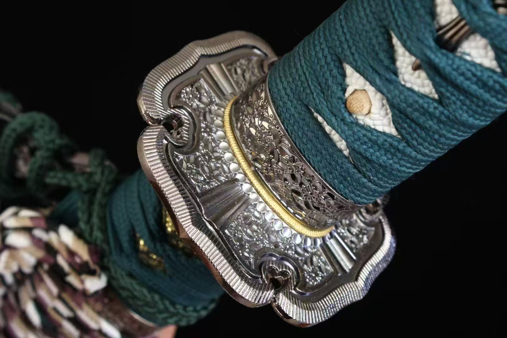 A detailed close-up of the ornate alloy fuchi (hilt collar) and the verdant green silk ito wrap.