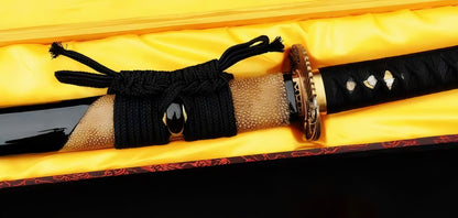 A detailed close-up of the Golden Hawk Katana, showcasing the gloss-black lacquer saya with its luxurious partial brown rayskin wrap, the black silk ito handle, and the brass "Golden Hawk" tsuba.