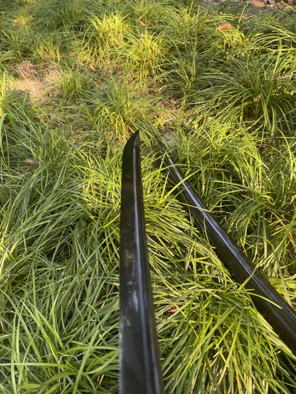 The complete Obsidian Edge Katana, fully sheathed in its gloss-black piano lacquer saya, resting in a grassy setting.