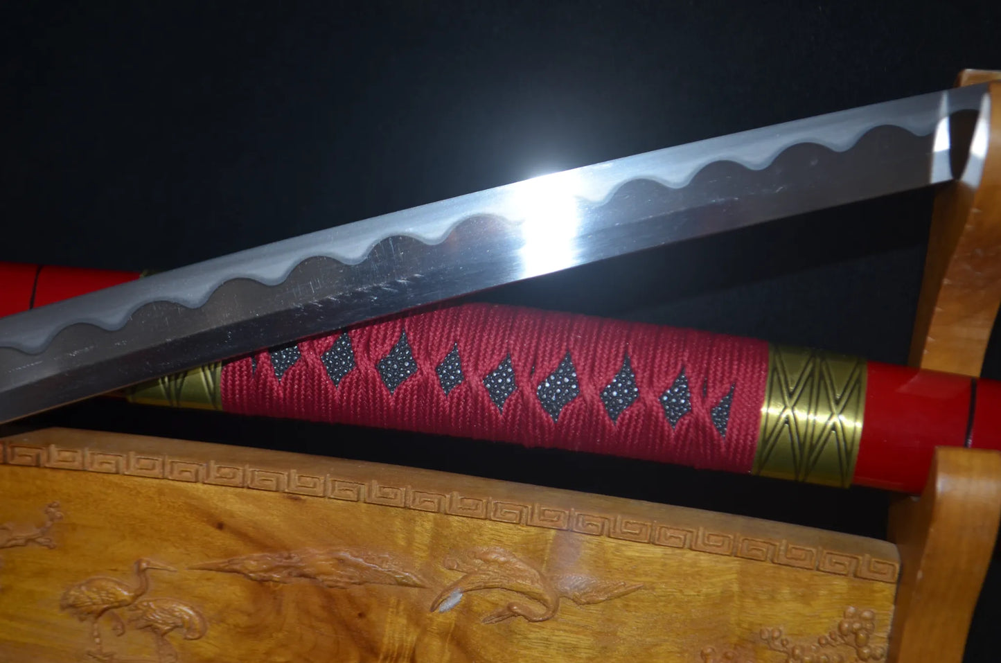 Mid-saya detail of the Sandai Kitetsu katana, showing the red cord wrap over black diamonds and gold accent rings on the glossy red saya.