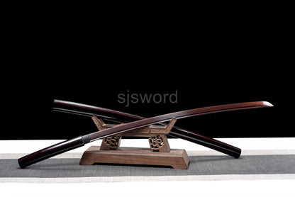 The unsheathed Aurora Steel Shirasaya with its red folded steel blade, crossed over the saya on a stand.