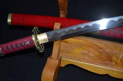 Close-up of the Sandai Kitetsu tsuka: red ito wrap over black rayskin, gold fuchi and the open-work gold tsuba at the blade's base.