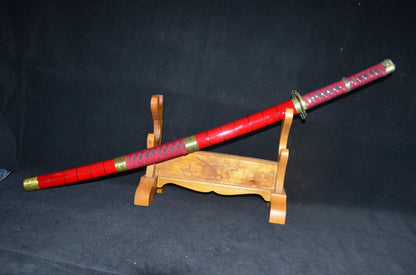 The Sandai Kitetsu "One Piece" katana sheathed in its glossy red saya with gold koiguchi and kojiri fittings, displayed on a carved wooden stand.