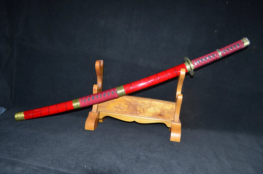 The Sandai Kitetsu "One Piece" katana sheathed in its glossy red saya with gold koiguchi and kojiri fittings, displayed on a carved wooden stand.