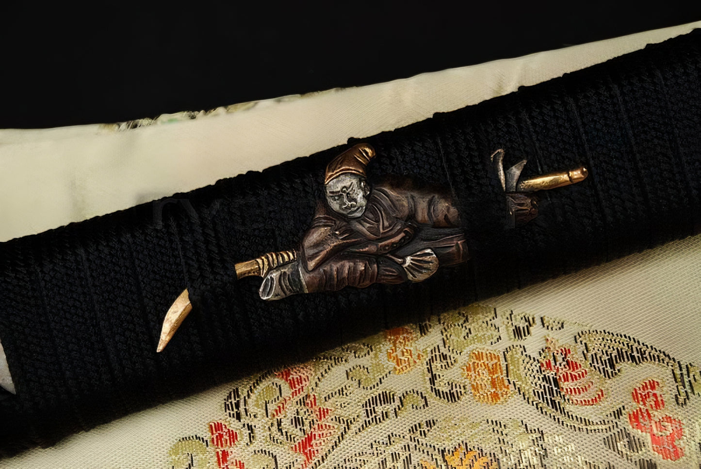 A detailed macro shot of the "Sennin" (Sage) theme menuki ornament on the black ito-wrapped handle of the Sennin's Guardian Katana.