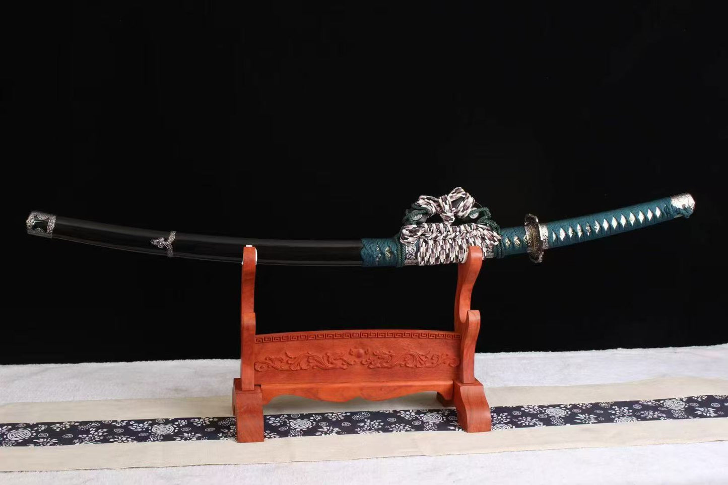 The complete Verdant Trace Tachi, fully sheathed in its hardwood saya, resting on an orange display stand.