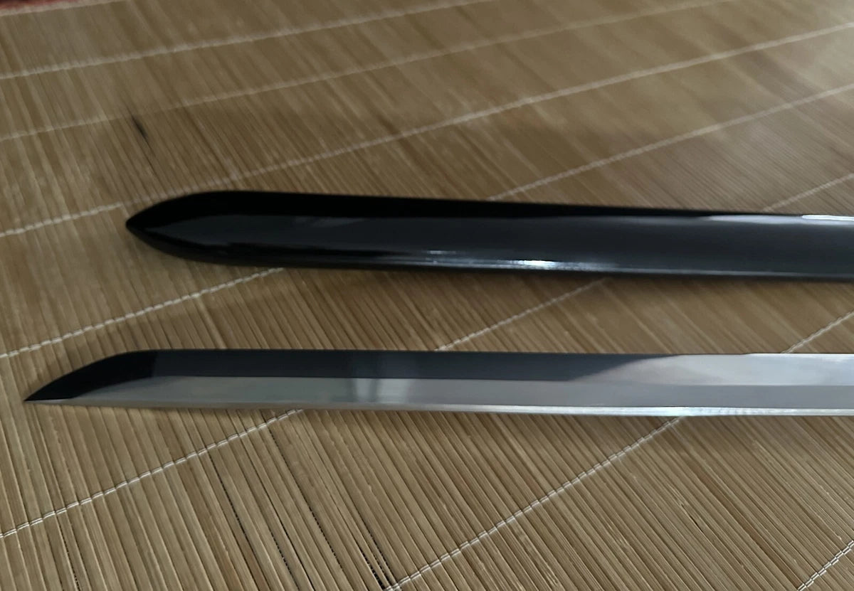 A view of the sharp kissaki tip of the straight blade alongside the gloss-black lacquered saya.