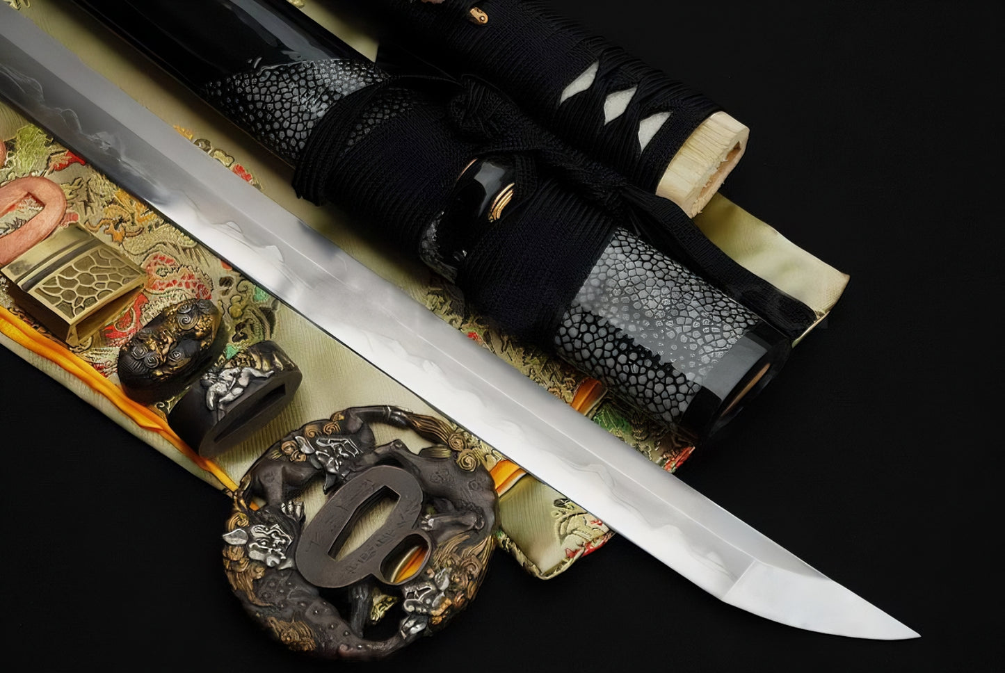A flat-lay display of the Sennin's Guardian Katana, showing the T10 clay-tempered blade, the "Shishi" theme fittings, and the partial rayskin wrapped saya.