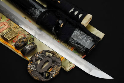 A flat-lay display of the Sennin's Guardian Katana, showing the T10 clay-tempered blade, the "Shishi" theme fittings, and the partial rayskin wrapped saya.