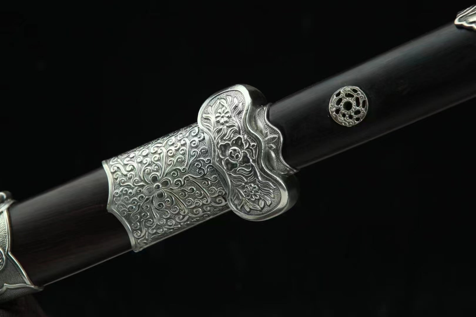 A detailed close-up of the General's Virtue Dao, showcasing the intricately carved white copper (Bai Tong) guard and scabbard mouth with its Peony & Scrollwork theme against the ebony wood.