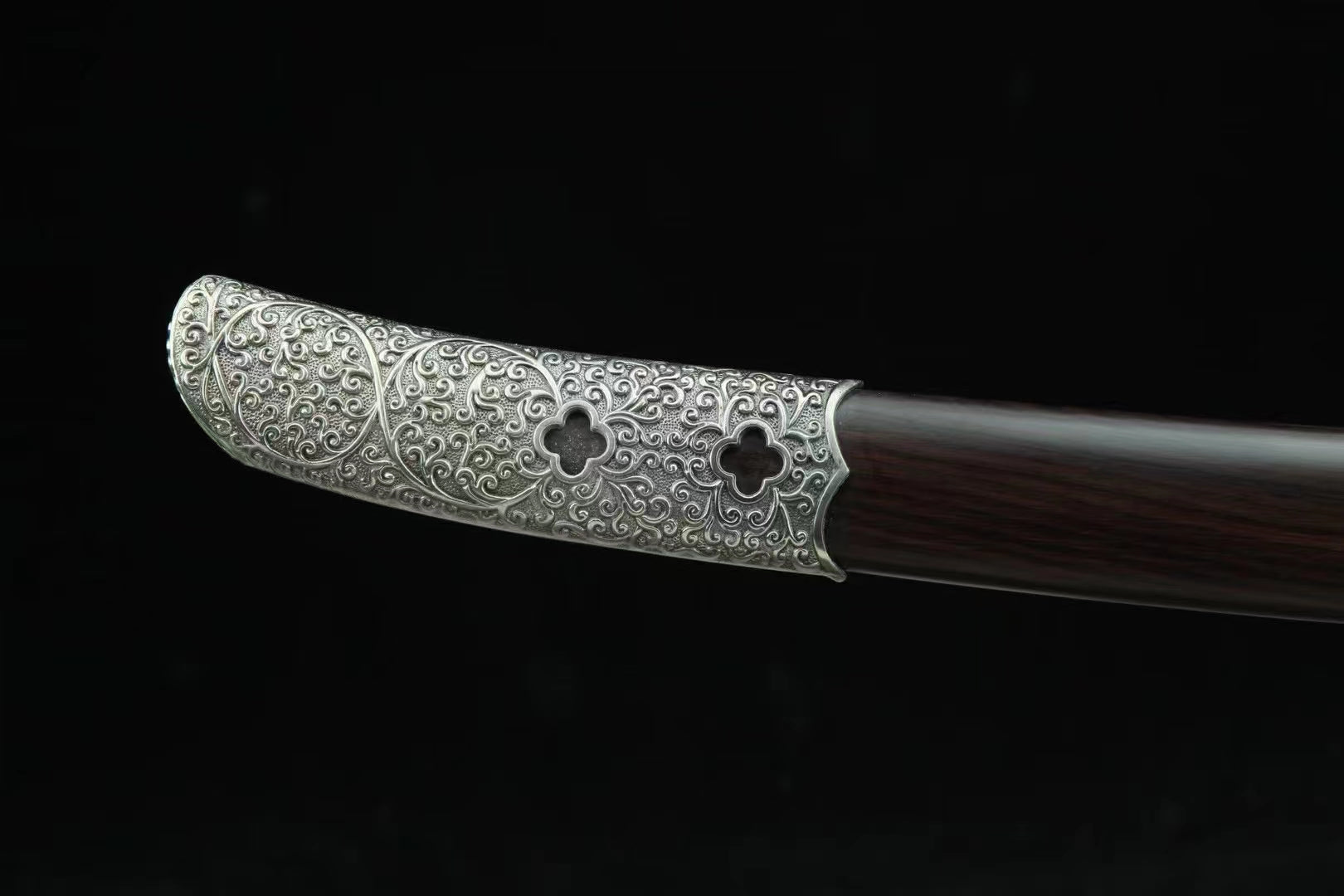 A macro shot of the General's Virtue Dao's scabbard tip (kojiri), featuring the large, ornate white copper (Bai Tong) mount with Peony & Scrollwork carvings on the ebony wood.